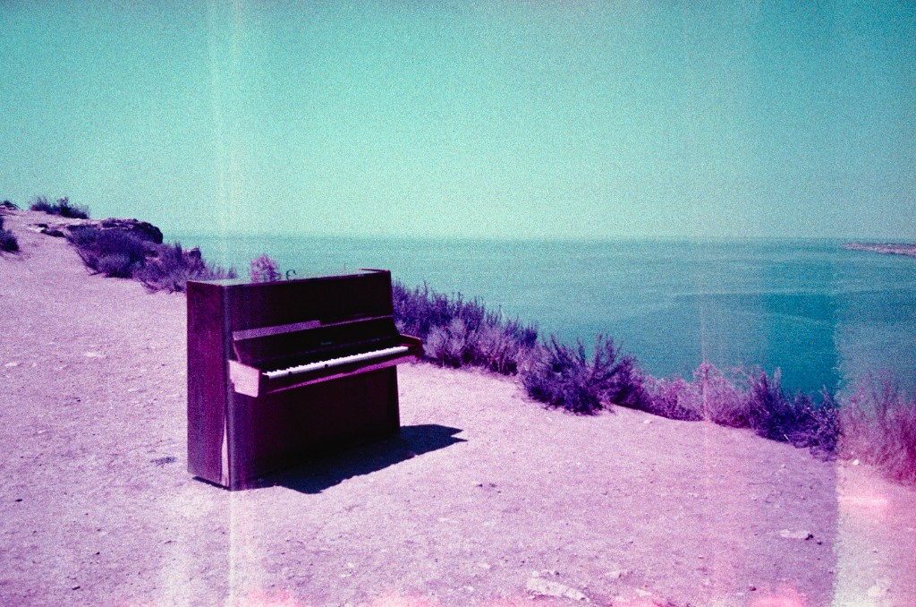 An upright piano standing on a seaside cliff under a cyan sky.